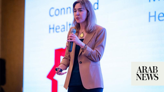 Dina Katabi standing on stage holding a microphone and a remote.