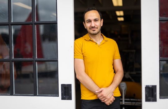 Portrait of Fadel Adib in a yellow polo leaning against a door.